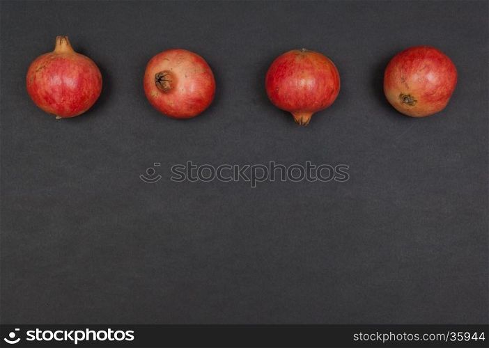 Whole ripe pomegranates in a row on dark grey background