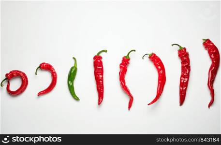 whole ripe red hot chili peppers on a white background, one green, concept of distinction and discrimination
