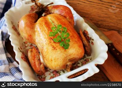 Whole roasted chicken in cooking casserole dish on wooden table. Whole roasted chicken in cooking casserole dish