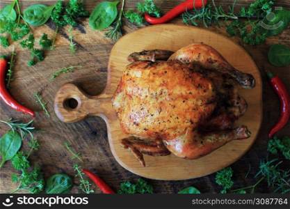 Whole roasted chicken with herb on cutting board . Top view .. Whole roasted chicken on cutting board. Top view