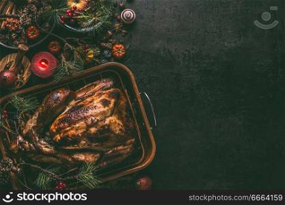 Whole roasted turkey, stuffed with dried fruits in roasting pan for Christmas dinner, served on dark table background with decoration and burning candles,  top view with copy space for your design