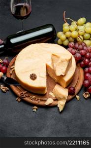 Whole round Head parmesan cheese, wine and grapeson wooden cutting board. Whole round Head parmesan cheese, wine and grapes