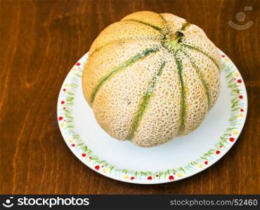 whole sicilian muskmelon (cantaloupe melon) on plate on wooden table