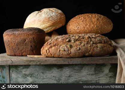 whole various baked rye flour bread rolls on an old wooden table, black background