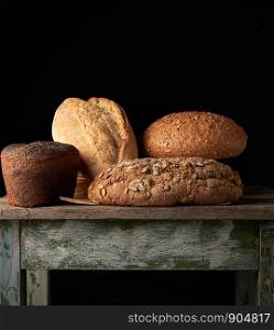 whole various baked rye flour bread rolls on an old wooden table, black background