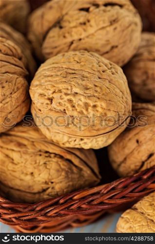 Whole walnuts in a wicker basket on rustic, wooden background