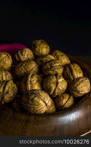 Whole walnuts piled in a wood bowl, nutcrackers on side, dark background, portrait from above, copyspace.
