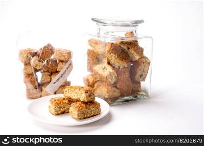 Whole wheat rusks on display in plastic bag, glass bottle and on white plate, on white isolated background.