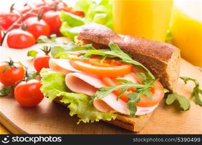 Wholegrain sandwich with ham, tomato, lattuce and arugula with glass of orange juice. Breakfast