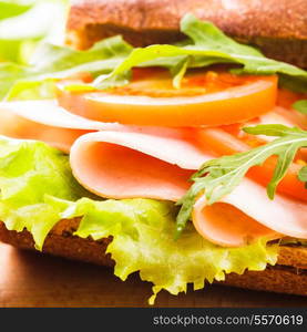 Wholegrain sandwich with ham, tomato, lattuce and arugula with glass of orange juice. Breakfast