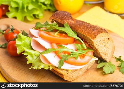 Wholegrain sandwich with ham, tomato, lattuce and arugula with glass of orange juice. Breakfast