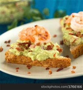 Wholegrain toast bread slices with guacamole, fried shrimp and fried bacon pieces (Selective Focus, Focus on the front of the shrimp on the bread)