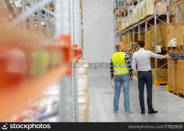 wholesale, logistic business and people concept - manual worker and businessman talking at warehouse. worker and businessman talking at warehouse