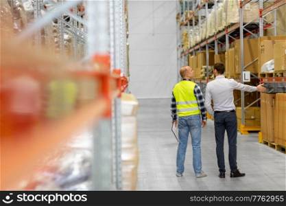 wholesale, logistic business and people concept - manual worker and businessman talking at warehouse. worker and businessman talking at warehouse