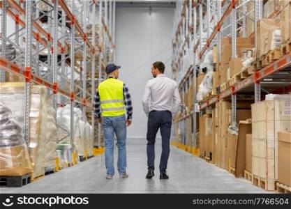 wholesale, logistic business and people concept - manual worker and businessman walking along warehouse. worker and businessman walking along warehouse