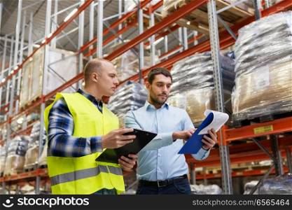 wholesale, logistic business and people concept - manual worker and businessman with clipboards at warehouse. worker and businessman with clipboard at warehouse