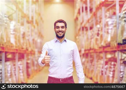 wholesale, logistic, business, export and people concept - happy man at warehouse showing thumbs up gesture