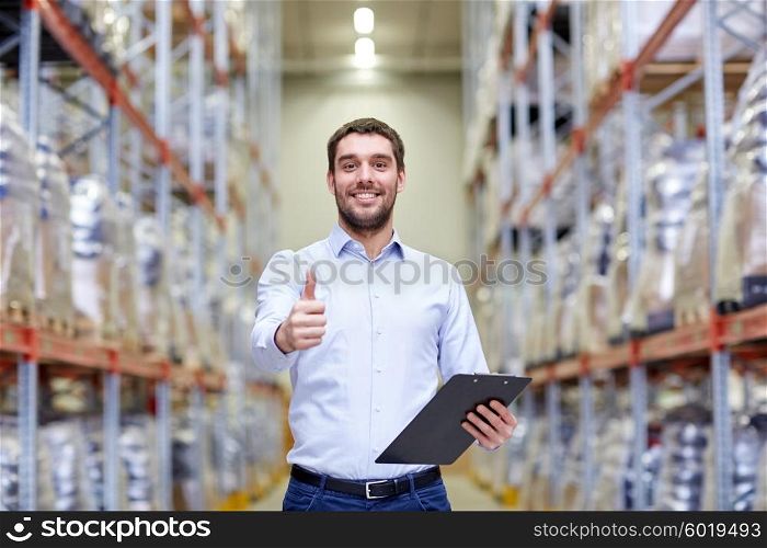 wholesale, logistic, business, export and people concept - happy man with clipboard at warehouse showing thumbs up gesture