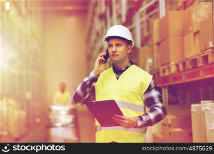 wholesale, logistic, business, export and people concept - man in hardhat and reflective safety vest with clipboard calling on smartphone at warehouse