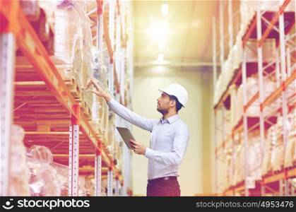 wholesale, logistic, business, export and people concept - man or manager in hardhat with tablet pc computer checking goods at warehouse. businessman with tablet pc at warehouse