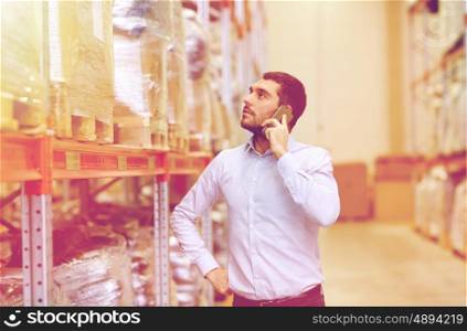 wholesale, logistic, business, export and people concept - serious businessman calling on smartphone at warehouse