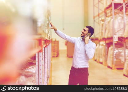 wholesale, logistic, business, export and people concept - smiling businessman calling on smartphone at warehouse. happy man calling on smartphone at warehouse