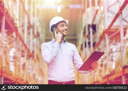 wholesale, logistic, business, export and people concept - smiling businessman with clipboard calling on smartphone at warehouse. man with clipboard and smartphone at warehouse