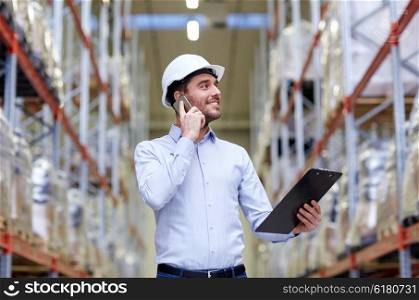 wholesale, logistic, business, export and people concept - smiling businessman with clipboard calling on smartphone at warehouse