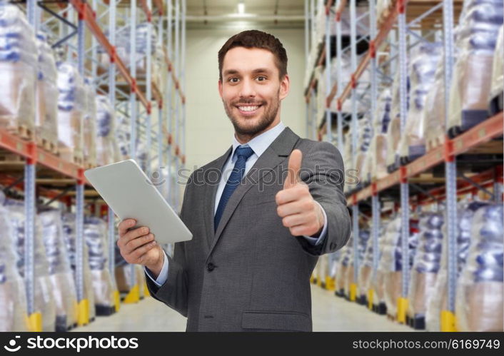 wholesale, logistic business, export, technology and people concept - smiling businessman with tablet pc computer showing thumbs up over warehouse background