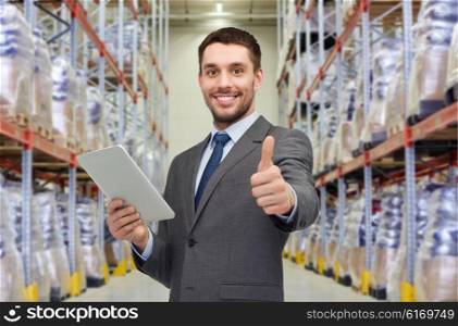 wholesale, logistic business, export, technology and people concept - smiling businessman with tablet pc computer showing thumbs up over warehouse background