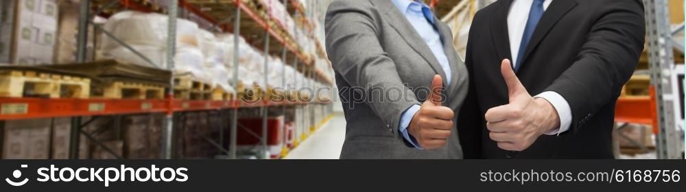 wholesale, logistic, international business, export and people concept - close up of man and woman showing thumbs up gesture over warehouse background
