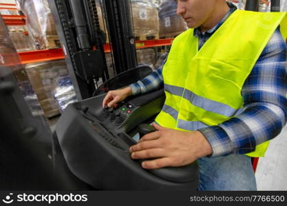 wholesale, logistic, loading, shipment and people concept - close up of man or worker operating forklift loader at warehouse. man operating forklift loader at warehouse