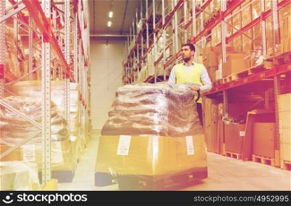 wholesale, logistic, loading, shipment and people concept - man carrying loader with goods at warehouse. man carrying loader with goods at warehouse