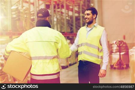 wholesale, logistic, people, agreement and export concept - manual worker and businessmen in reflective safety vests shaking hands and making deal at warehouse