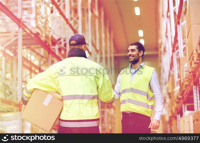 wholesale, logistic, people, agreement and export concept - manual worker and businessmen in reflective safety vests shaking hands and making deal at warehouse. men in safety vests shaking hands at warehouse