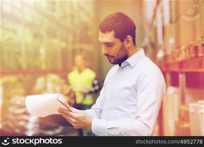 wholesale, logistic, people and export concept - businessman or supervisor with clipboards at warehouse. businessman writing to clipboard at warehouse