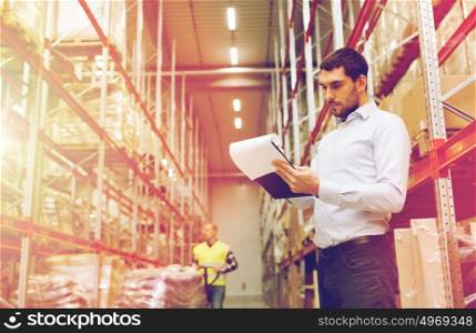 wholesale, logistic, people and export concept - businessman or supervisor with clipboards at warehouse. businessman writing to clipboard at warehouse