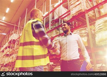 wholesale, logistic, people and export concept - manual worker and businessmen with clipboard shaking hands and making deal at warehouse. worker and businessmen with clipboard at warehouse