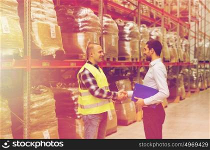 wholesale, logistic, people and export concept - manual worker and businessmen with clipboard shaking hands and making deal at warehouse. worker and businessmen with clipboard at warehouse