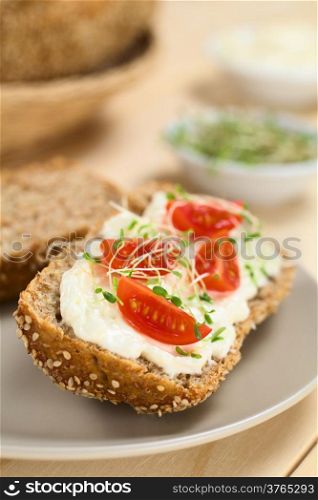 Wholewheat bread spread with cream cheese, with cherry tomato and alfalfa sprouts on top served on plate (Selective Focus, Focus on the tomato in the front)