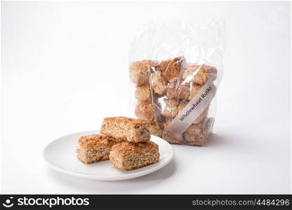 Wholewheat rusks stacked in a plastic bag as well as some on a plate on a white background.