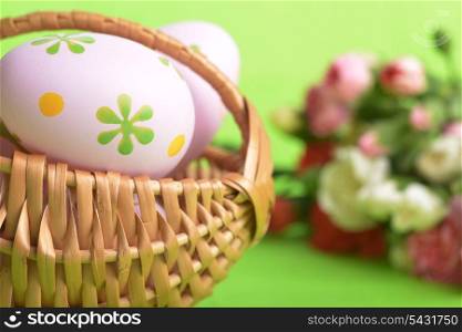 wicker basket of easter eggs with flowers carnation on green background
