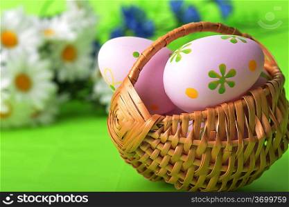 wicker basket of easter eggs with wildflowers on green background