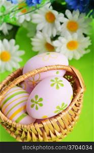 wicker basket of easter eggs with wildflowers on green background