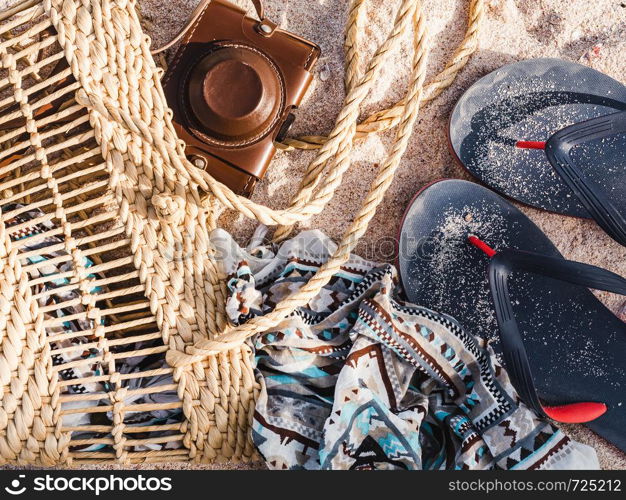 Wicker basket, vintage camera and shawl on sand background. Top view, close-up. Wicker basket, vintage camera and shawl on sand