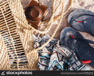 Wicker basket, vintage camera and shawl on sand background. Top view, close-up. Wicker basket, vintage camera and shawl on sand