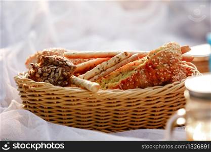 Wicker basket with bread. Bread, buns and grissini inside basket. Fresh bakery products on picnic. selective focus.. Wicker basket with bread. Bread, buns and grissini inside basket. Fresh bakery products on picnic. selective focus