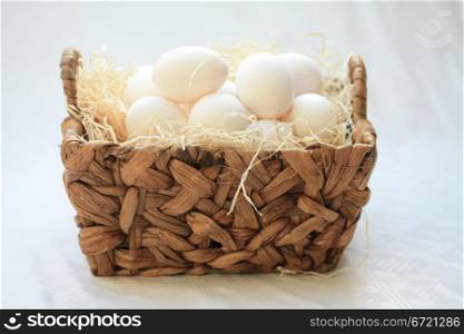 Wicker basket with hay and white eggs