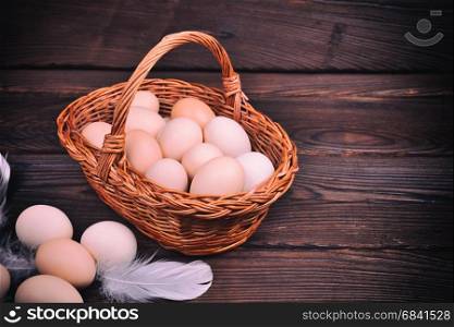 Wicker basket with raw chicken eggs on a brown wooden background, empty space on the right