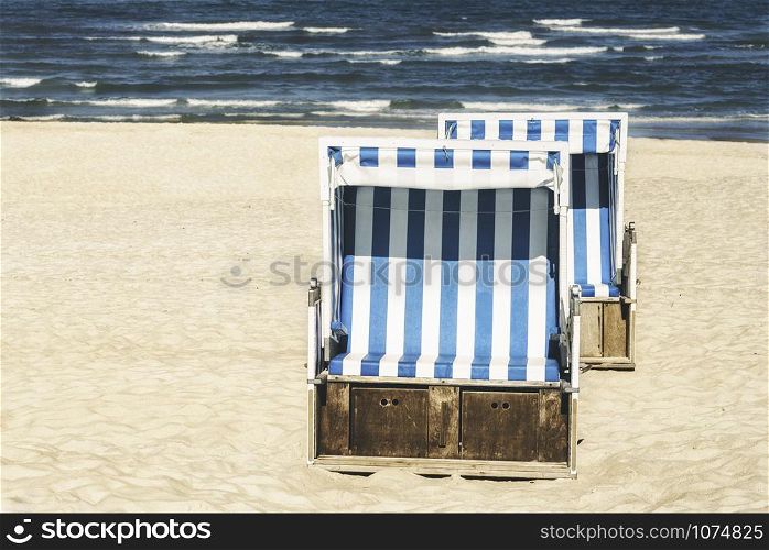 Wicker beach chairs on white sand at North Sea, on Sylt island, in Germany. Summer vacation with blue water, waves and beach chairs. Sunny beach day